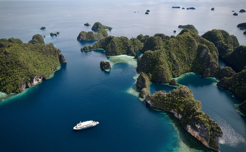 Aerial view of Kudanil Explorer yacht cruising through the turquoise waters of Raja Ampat, Indonesia.