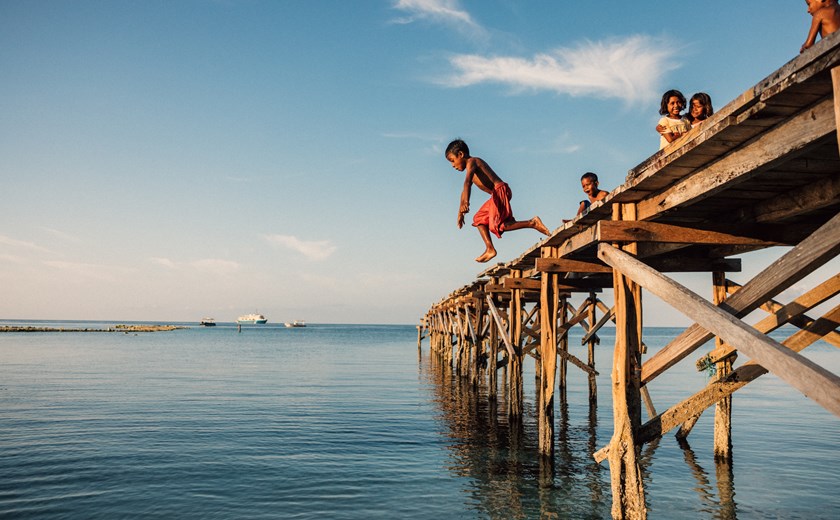 Children enjoying a fun swim and dive into crystal-clear Indonesian waters under the sun.