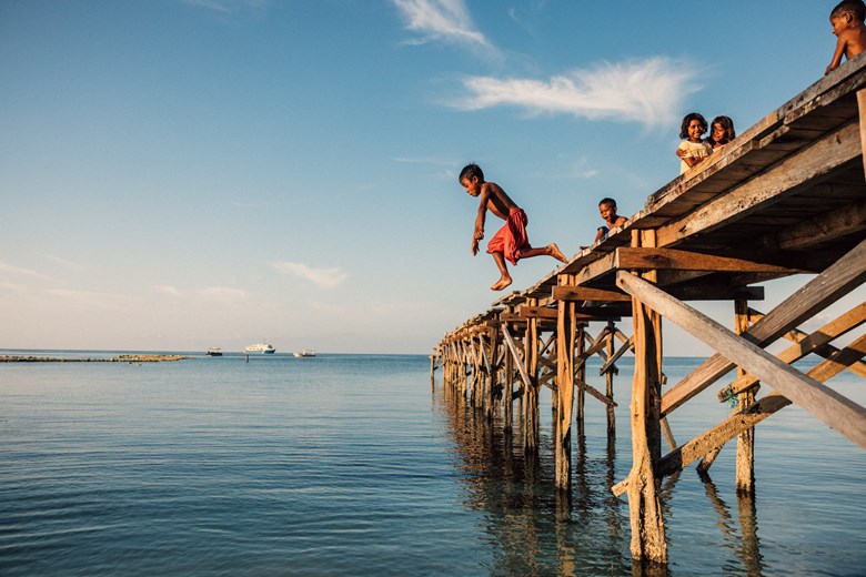 Children enjoying a fun swim and dive into crystal-clear Indonesian waters under the sun.