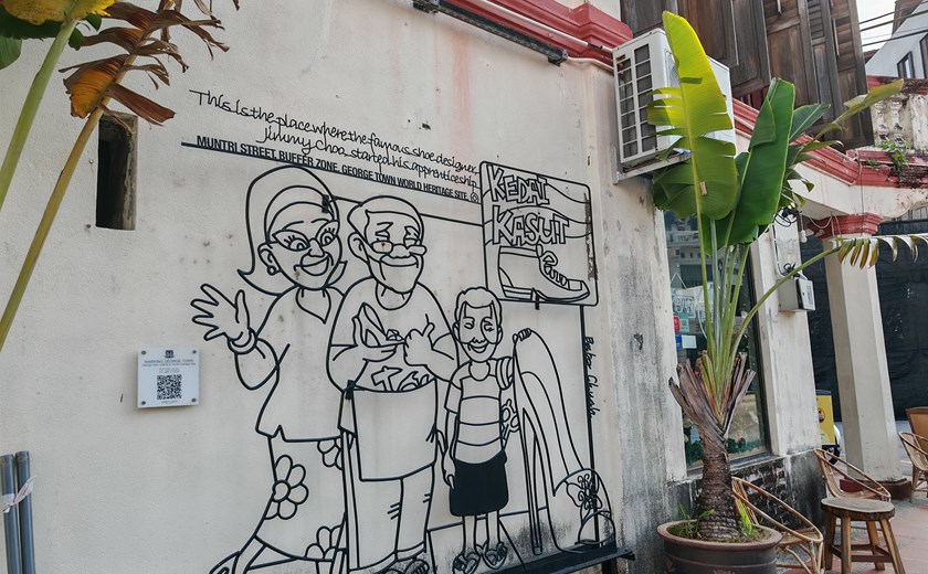 Wall mural in George Town, Penang, depicting a cartoon-style family and street scene, painted in black on a white wall.