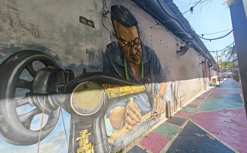 Street mural in George Town, Penang showing a man using a traditional sewing machine